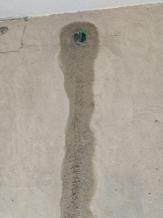 Multifix-dosa installerad i betongvägg, omgiven av nylagt lagningsbruk. Dosan är grön med rörspår synliga neråt.