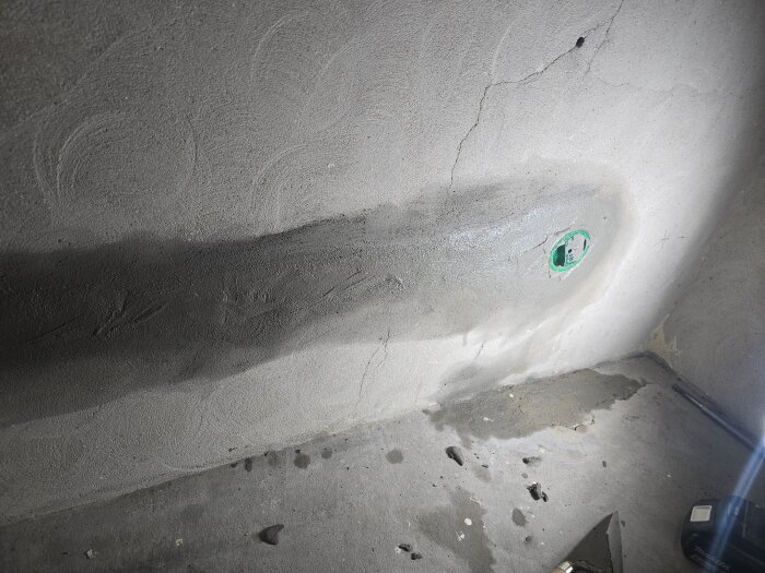 Vägg med spår i betong och en nyinstallerad elektrisk dosa, omgiven av verktyg och sprickor i väggen.