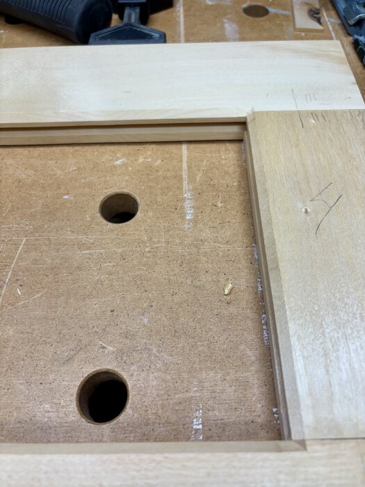 45-graders fasad träfog i ett hörn på en arbetsbänk, användning av fräsverktyg för träbearbetning, med synliga hål i bänken.