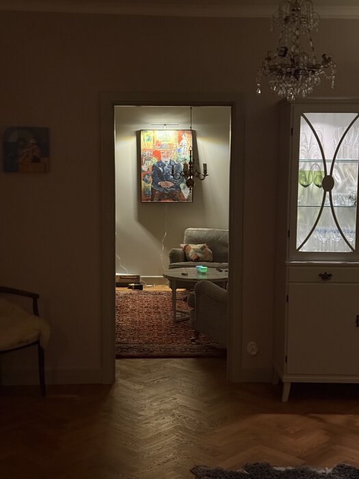 Vy in i ett vardagsrum med soffa, färgglad tavla på väggen, ett litet bord och en persisk matta. Hängande lampa i taket.