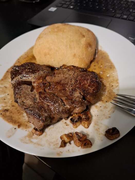 Tallrik med entrecôte, ciabatta och svamp vid en dator.