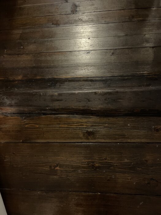 Mörkt trägolv med tydliga brädor och en tröskel; rummen renoverade med synligt drag längs tröskeln.