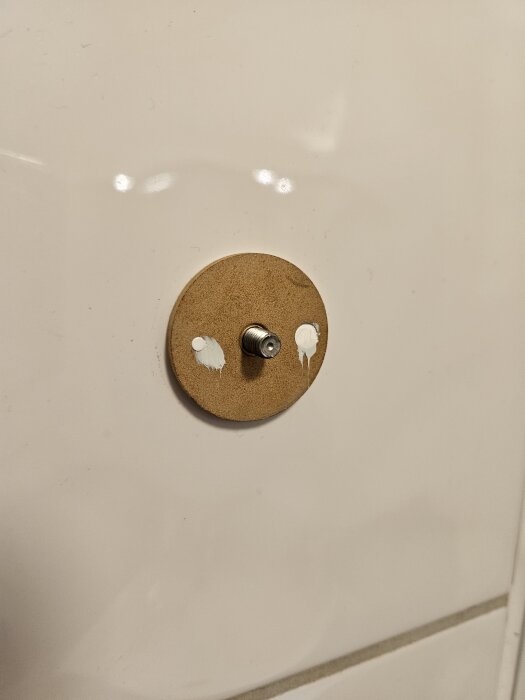 Limrester på en vit kakelvägg där en handdukskrok har avlägsnats, med skruvfäste synligt.