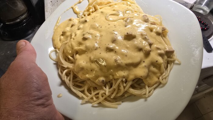 Tallrik med spaghetti toppad med krämig sås, serverad på ett köksbord.