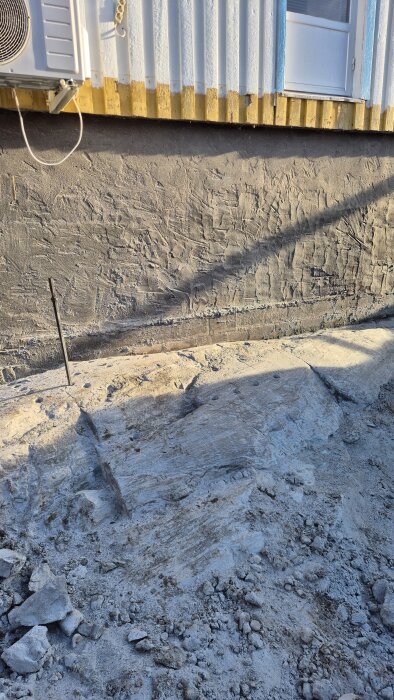 Borrad berggrund intill husvägg, hål för snigeldynamit synliga.