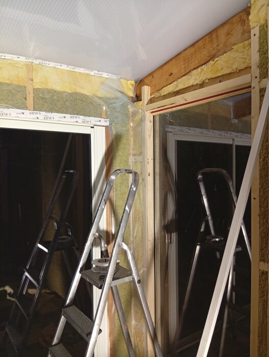 Stege står i ett halvfärdigt uterum med isolering synlig i väggarna och plast installerad i taket.