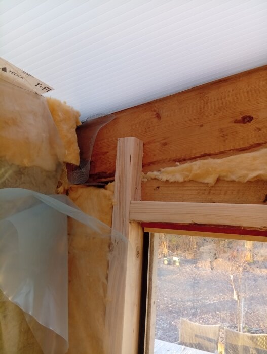 Isolering och plastfolie vid en takstol i ett pågående uterumsprojekt med trävägg och kanalplasttak.