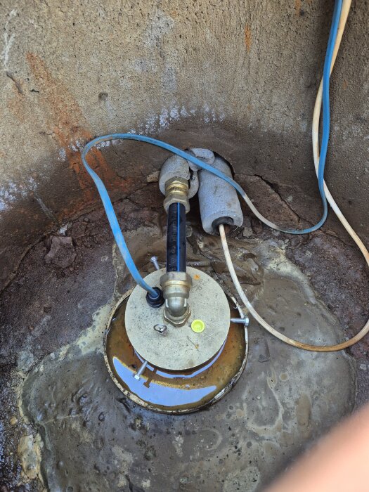 Nedgrävd röranslutning i betongmiljö med synliga kablar och metallkomponenter. Risk för att frysa under vintern.