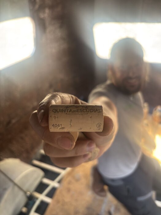 En person håller fram en vinkork från Quinta do Escudial inne i ett rum med två fönster i bakgrunden.