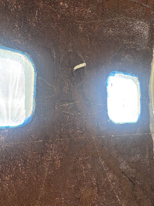 Vägg med påbörjat korkmönster framför fönster där korkarna limmas för solnedgångsdesign; synliga skisser förväntas utvecklas vidare.