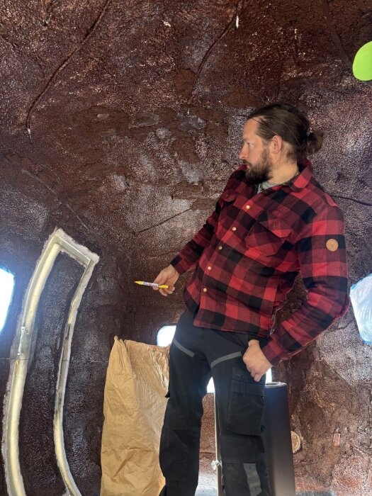 Person i rutig skjorta skissar på väggen i en vagndel täckt med korkliknande material. Ljusinsläpp från fönster och öppnad dörr.