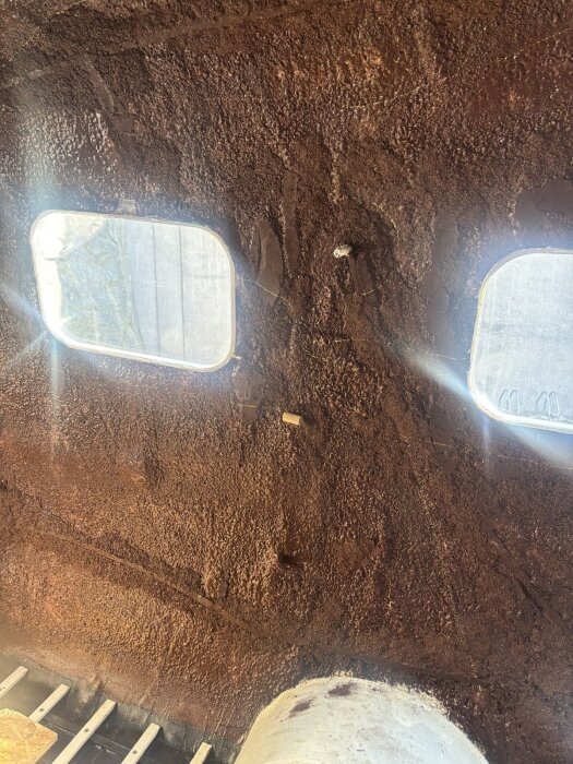 Rustik vägg inuti en vagn med två fönster och textur av kork, fångar ljuset från fönstren och skapade mönster av moln och reflektioner av solnedgång.