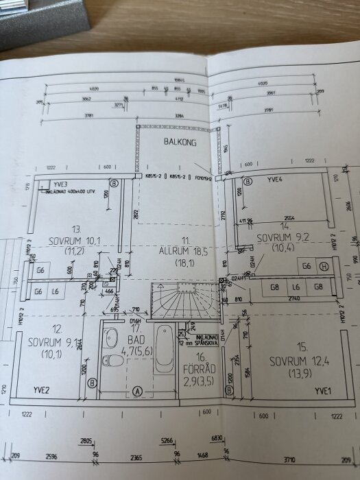 Ritning av bottenplan som visar olika rum, mått och eventuell information om bärande väggar. Uppställd på ett bord med en bok i bakgrunden.