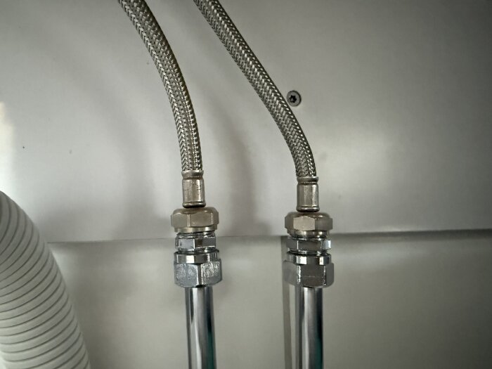 Flexibla metallslangar kopplade till vattenledningar under ett handfat; den vänstra slangen är för kort för att nå det högra röret.