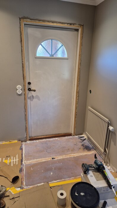 Ingång med oavslutad tröskel, synliga flytspacklade golv och verktyg för renovering. Golvvärmesystem nyligen installerat.