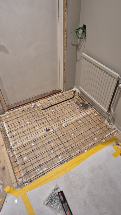 Golvyta med nylagt golvvärme och flytspackel, synlig trådnät och membran i en entré, förberett för vidare renovering.