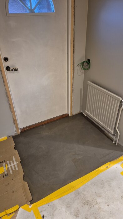 Flytspacklat golv i hall med golvvärme, dörr och element synliga.