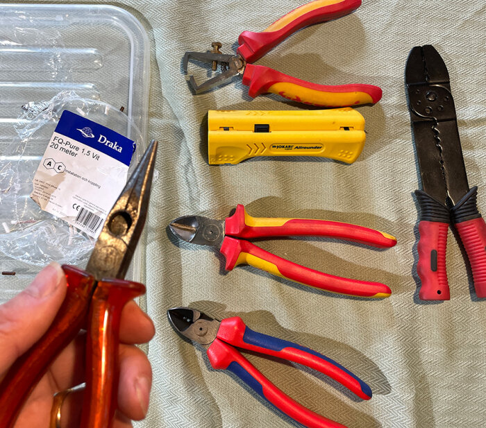 Olika skaltänger och en kabelsax liggandes på en beige yta, inklusive en Jokari-verktyg, bredvid en Draka kabelrulleetikett.