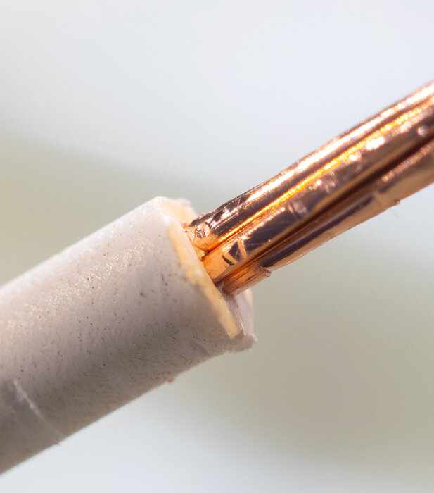 Närbild på en delvis skalad elektrisk kabel med koppartrådar synliga, vinkel från sidan.