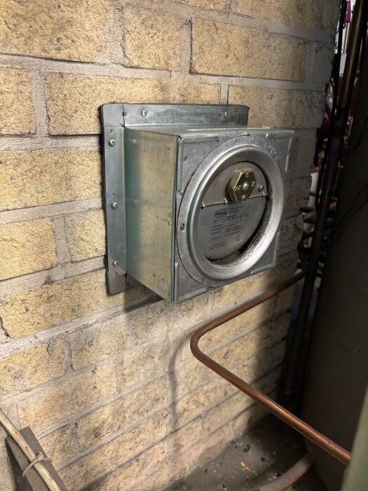 Dragbegränsare monterad på en tegelvägg över en tidigare rökrörsanslutning, med anslutande kopparrör.