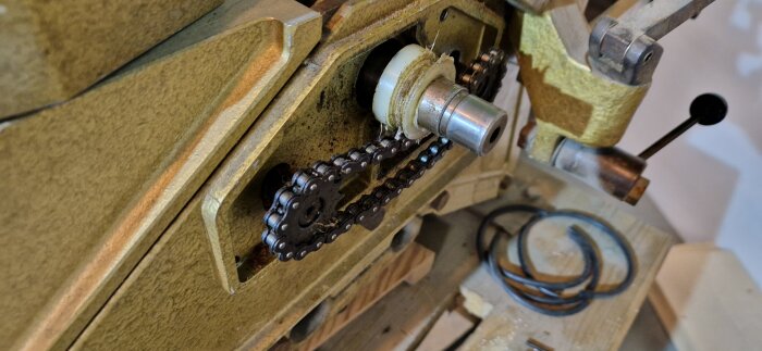 Närbild på en maskindel med en kedja och en smält plastring runt en axel, delvis isärplockad för inspektion och reparation.