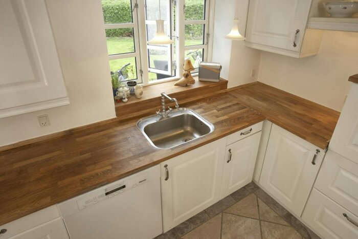 Köksbänk i U-form med träyta och diskho i mitten under två fönster, med olika överhäng på kortsidorna.