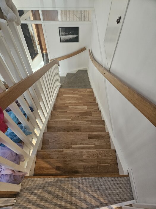 Trappa under renovering med trästeg och vita räcken, första svängda steget syns, taget uppifrån med synligt trappräcke.