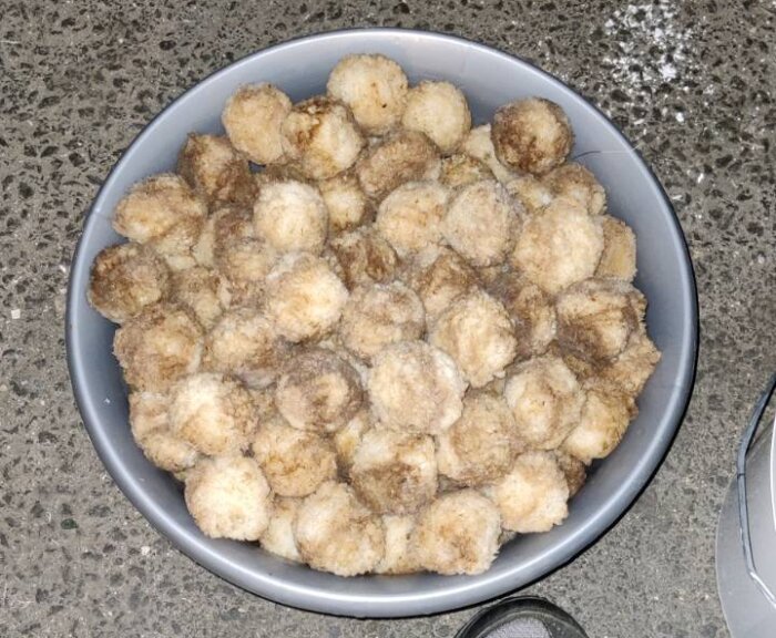 En skål fylld med brunvita filterbollar som används för att rena vatten i en badtunna, placerad på ett betonggolv.