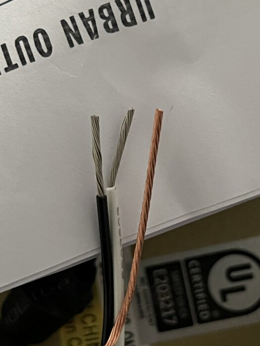 Tre elkablar, svart, vit och kopparfärgad, som löper parallellt mot en bakgrund av papp med text.