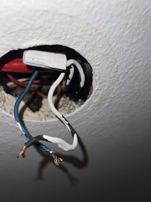 Två blottade elkablar, en svart och en blå, hänger från ett takuttag med ett vitt kopplingsdon synligt bredvid.