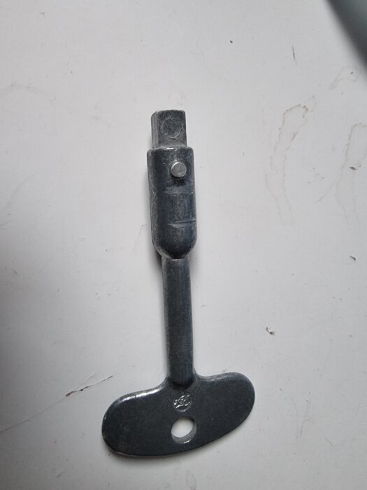 Nyckel till vindslucka i metall med T-format handtag och fyrkantig ända.