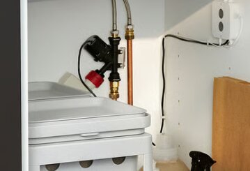 Vattenrör och en diskmaskinsavstängning under diskbänken, med anslutning till inkommande kallvatten och eluttag synliga i bakgrunden.