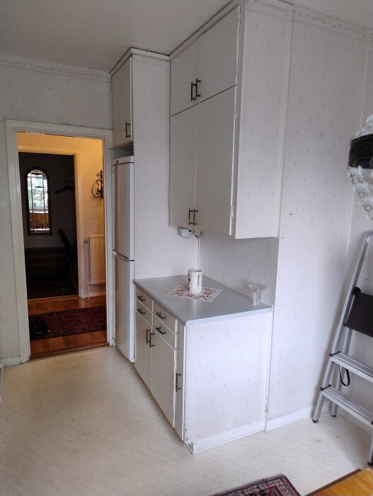 Vit köksvägg med skåp och bänk, en gång synlig i bakgrunden.