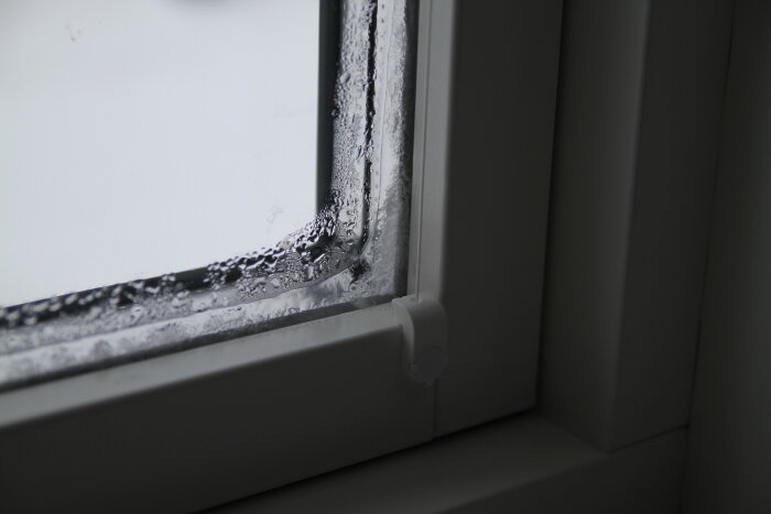 Fönster med isbildning på insidan, visar kondens och frost på ett modernt 3-glas fönster under kallt väder.