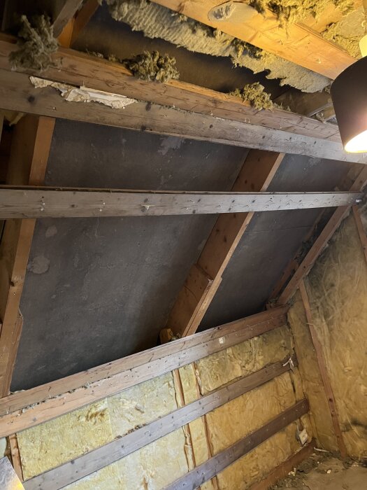 Ett rum med synliga träreglar och isolering på väggar och tak, där gipsskivor har rivits bort för att skapa en luftspalt.