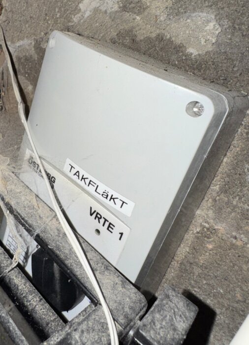 Takfläktens ventilationskåpa märkt Östberg VRTE 1, monterad mot en stenvägg, omgiven av dammiga ytor och elkablar.
