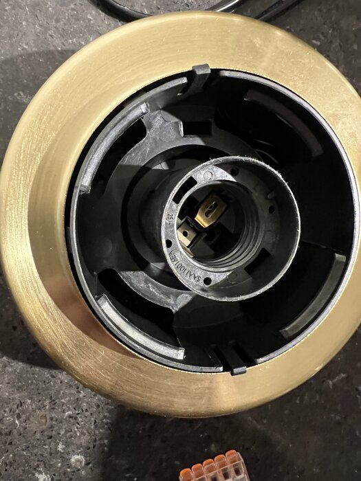 Närbild av en lampkontakt med en gyllene ring på ett mörkt underlag och en transparent anslutningsklämma bredvid.