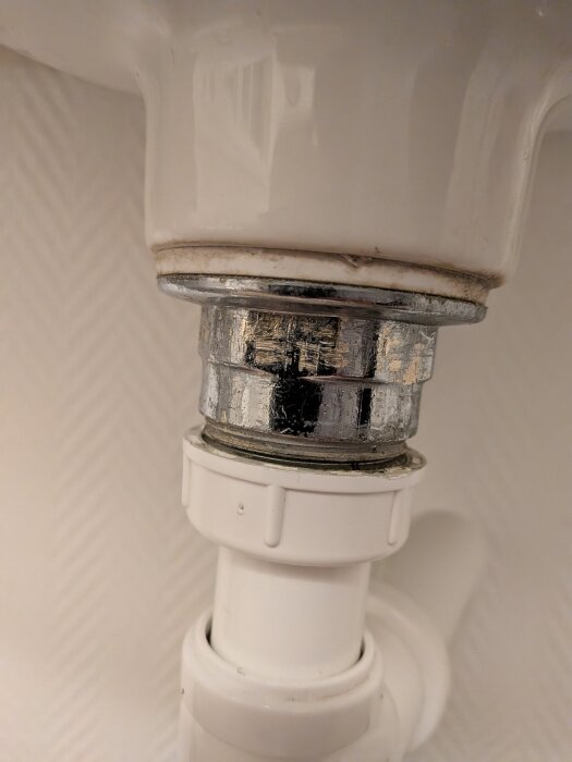 Bottenventil i ett äldre handfat med synliga metall- och plastdelar, där användaren har problem att lossa delarna.