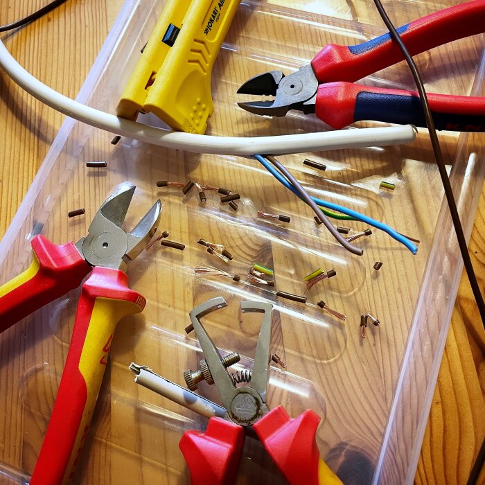 Avskalade elkablar och verktyg på ett bord, inklusive avbitartång och kabelskalare.