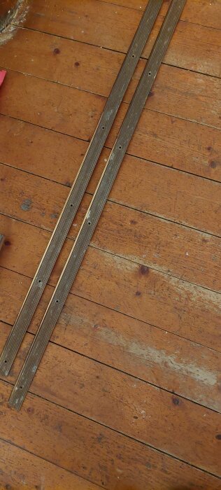 Mässing trappkantlister på ett trägolv, borttagna för rengöring under inomhusrenovering.