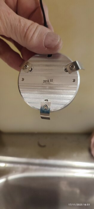 Rund skåpslampa med monteringsfästen och kabel, hålls i hand över diskbänk.