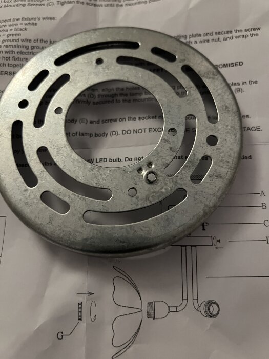 Metallisk monteringsplatta placerad över instruktionspapper med text och diagram.