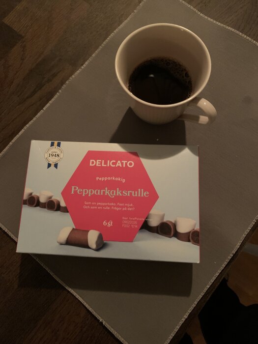 Förpackning med Delicato pepparkaksrulle och en kopp svart kaffe på ett bord.