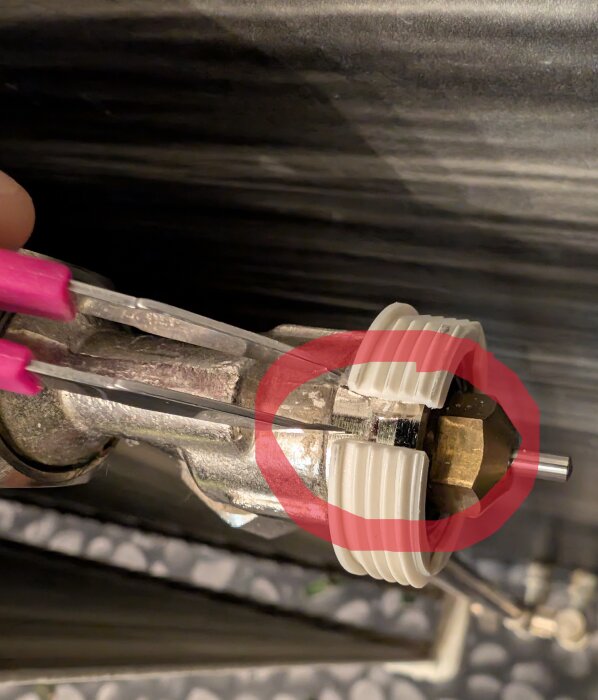 Radiatorventil med en RAVL-adapter som är för liten, markerad med en röd cirkel och hålls med en pincett.