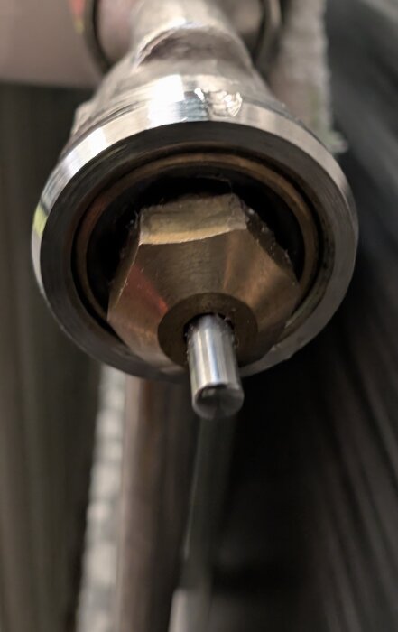 Närbild på en radiatorventil av okänd typ med en synlig axel, där en adapter inte fäster korrekt, markerad av en röd cirkel.