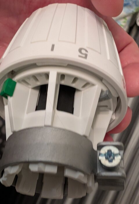 Danfoss-termostat med vit ratt och siffra 5, visad i närbild; monterad med metallklämma och skruv ovanpå en hand.