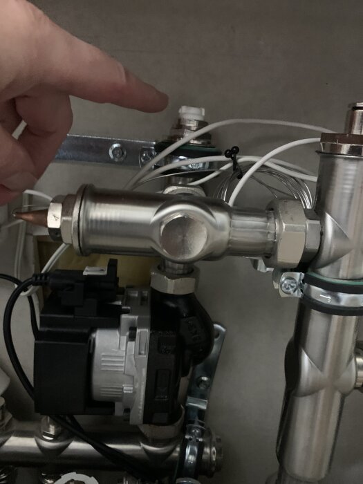 En hand pekar mot en ventil på ett rörsystem under diskussion om luftning.