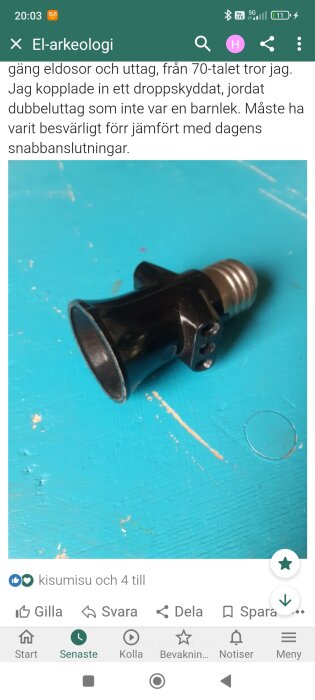 En svart eladapter eller lamphållare med en skruvkoppling ligger på ett blått bord.