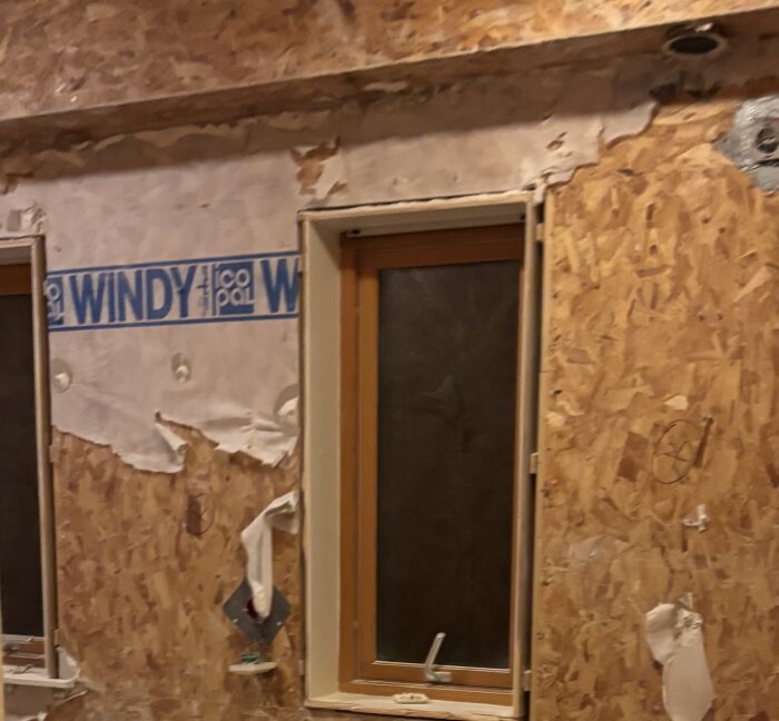 Vägg under renovering med fönster och byggplast med texten "WINDY".