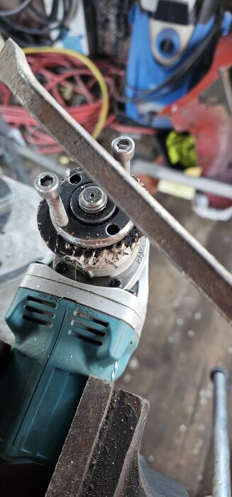 Vinkelslip med trasig spärr, två långa bultar och en skiftnyckel använd för att dra upp skivan som fastnat, i en verkstadsmiljö.